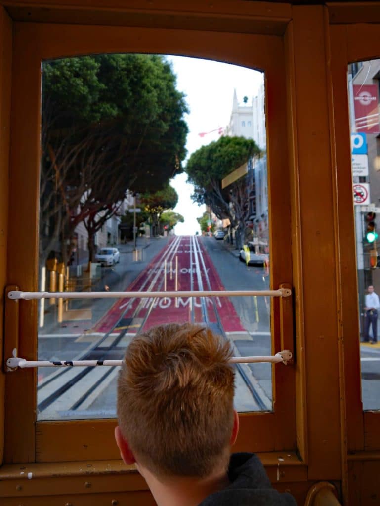 kind-sitzt-im-cable-car-und-blickt-aus-holzfenster-auf-die-huegelige-strasse-in-san-francisco