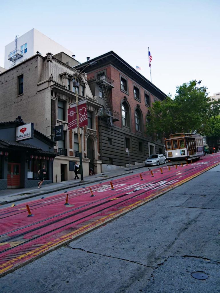 cable-car-faehrt-auf-huegeliger-rot-markierter-strasse-in-san-francisco