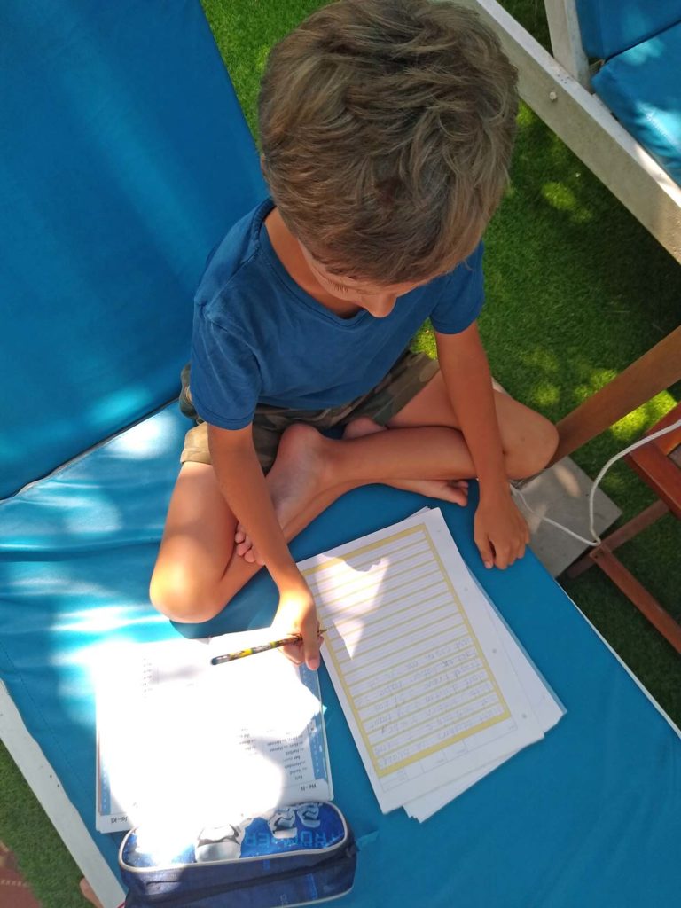 kind-schreibt-im-Arbeitsheft-am-Pool-homeschooling-unterricht-auf-reisen-weltreise-mit-kindern