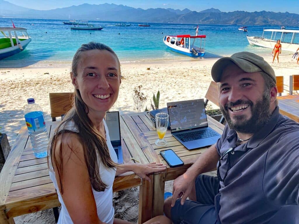 ehepaar-sitzt-mit-laptop-am-tisch-am-strand-mit-blick-auf-das-meer