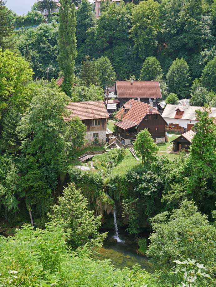 Plitvicer Seen mit Kindern - der schönste Nationalpark Kroatiens haeuser-in-gruener-landschaft-am-wasserfall-rastoke-kleiner-bruder-plitvicer-seen-kroatien