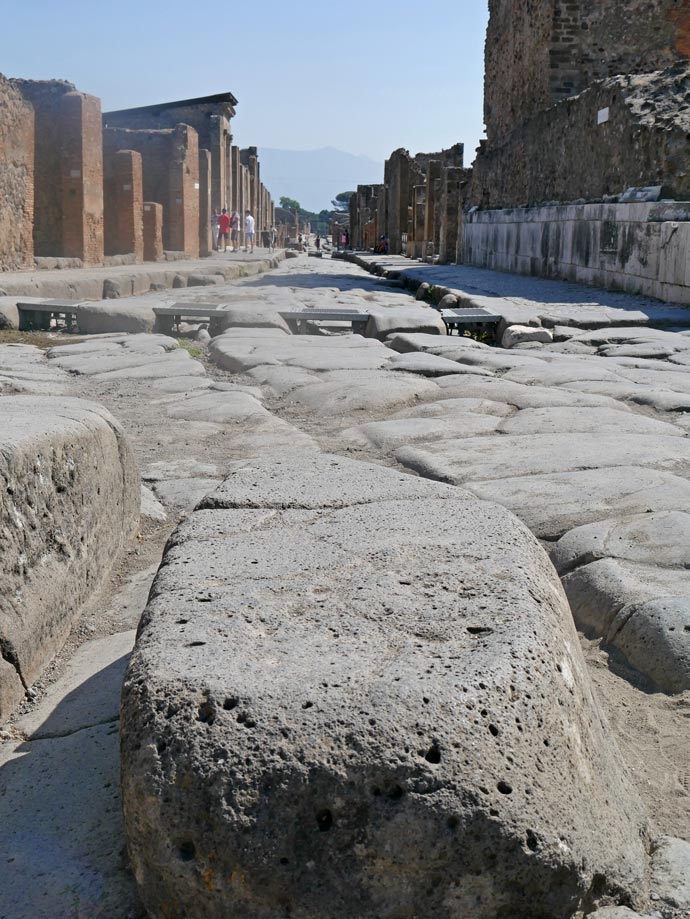 trittsteine-auf-roemischer-strasse-in-pompeji-mit-blick-auf-ruinen