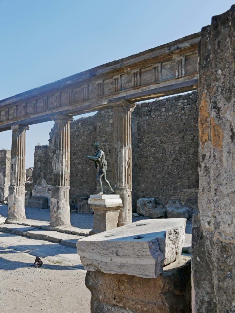 roemische-statue-vor-saeulen-in-roemischer-ausgrabungsstaette-pompeji