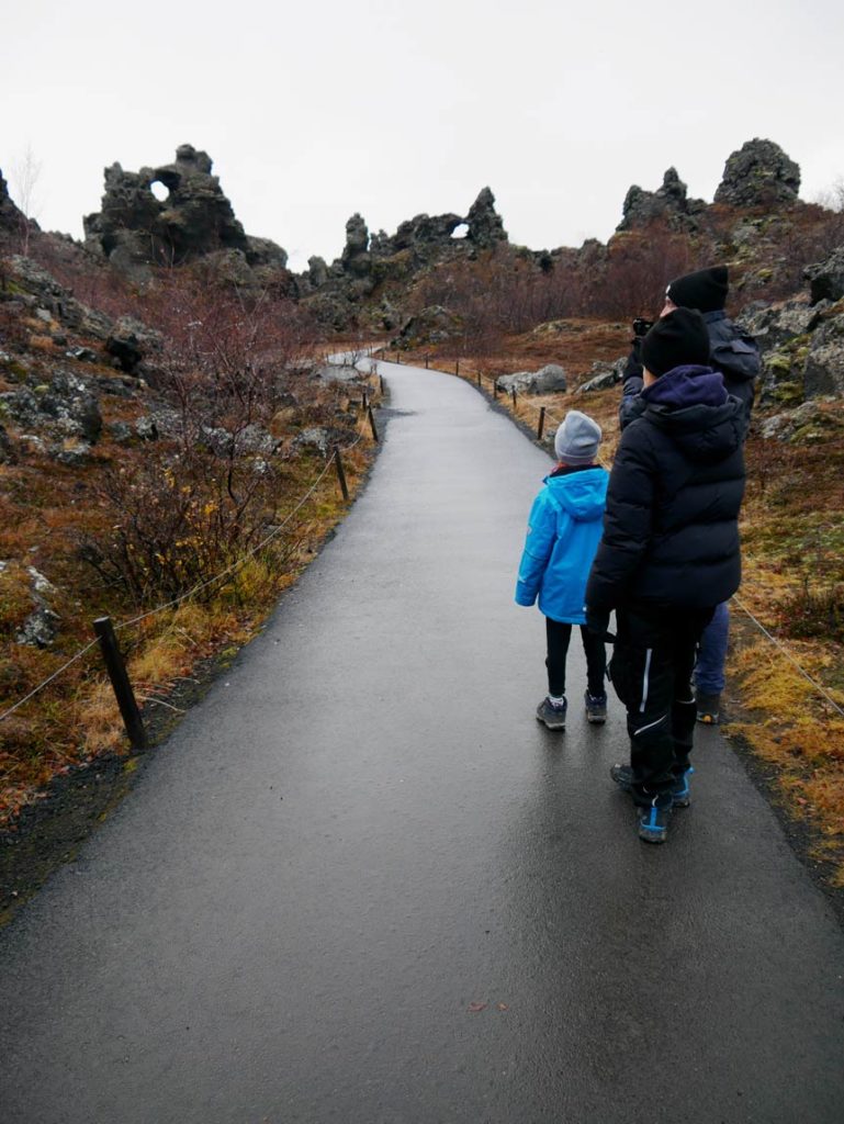 16 Nordisland Sehenswürdigkeiten, die ihr nicht verpassen dürft! dimmuborgir-lavafeld-zwei-kinder-laufen-auf-geteertem-weg-in-richtung-lavaformationen