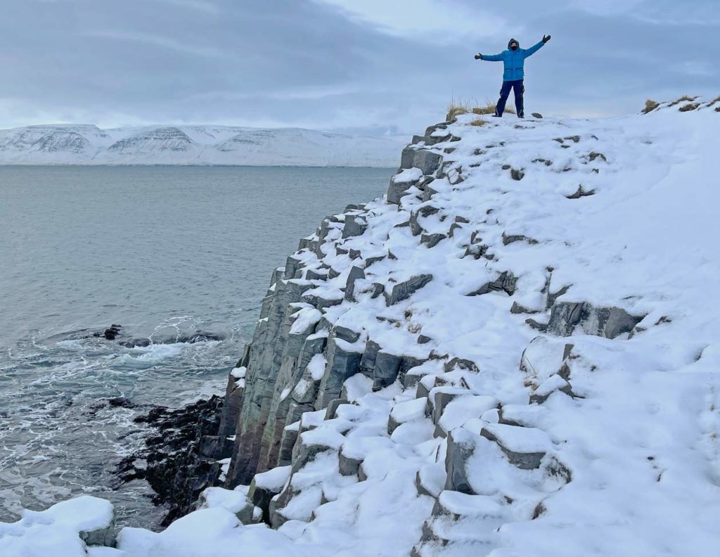 16 Nordisland Sehenswürdigkeiten, die ihr nicht verpassen dürft! mann-steht-auf-verschneiten-basaltsaeulen-am-meer-in-nordisland
