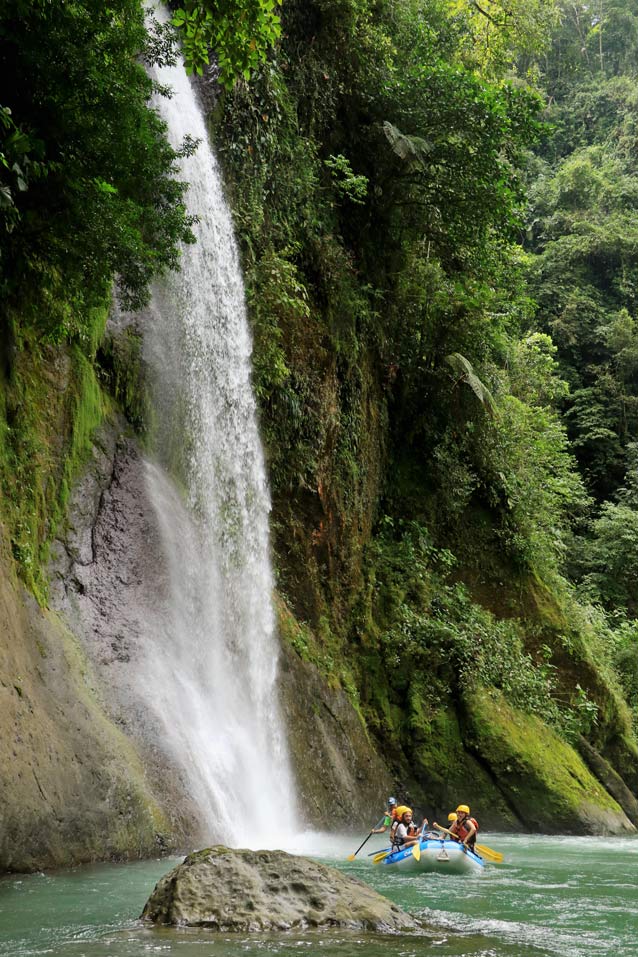 familie-im-blauen-rafting-boot-an-wunderschoenem-hohen-wasserfall-in-gruener-dschungel-landschaft-auf-dem-fluss