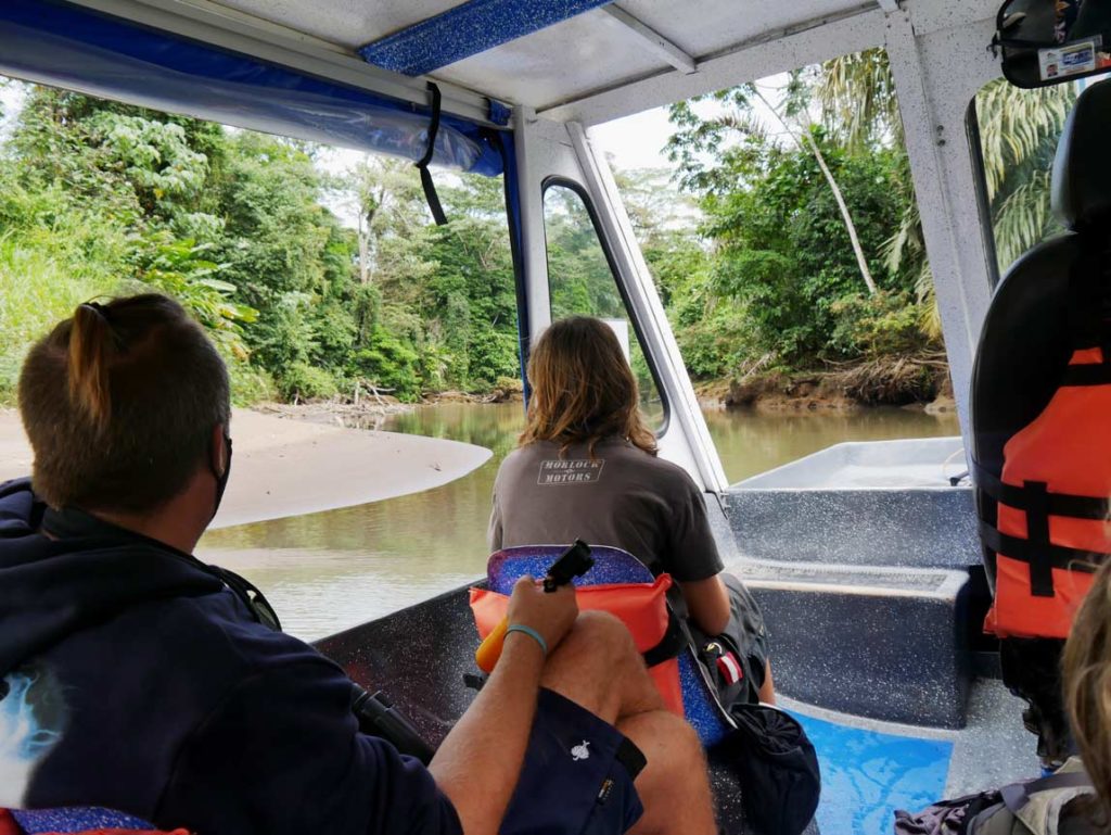 familie-sitzt-auf-stuehlen-in-kleinem-boot-im-tortuguero-nationalpark-in-costa-rica-und-fahert-ueber-braunen-fluss