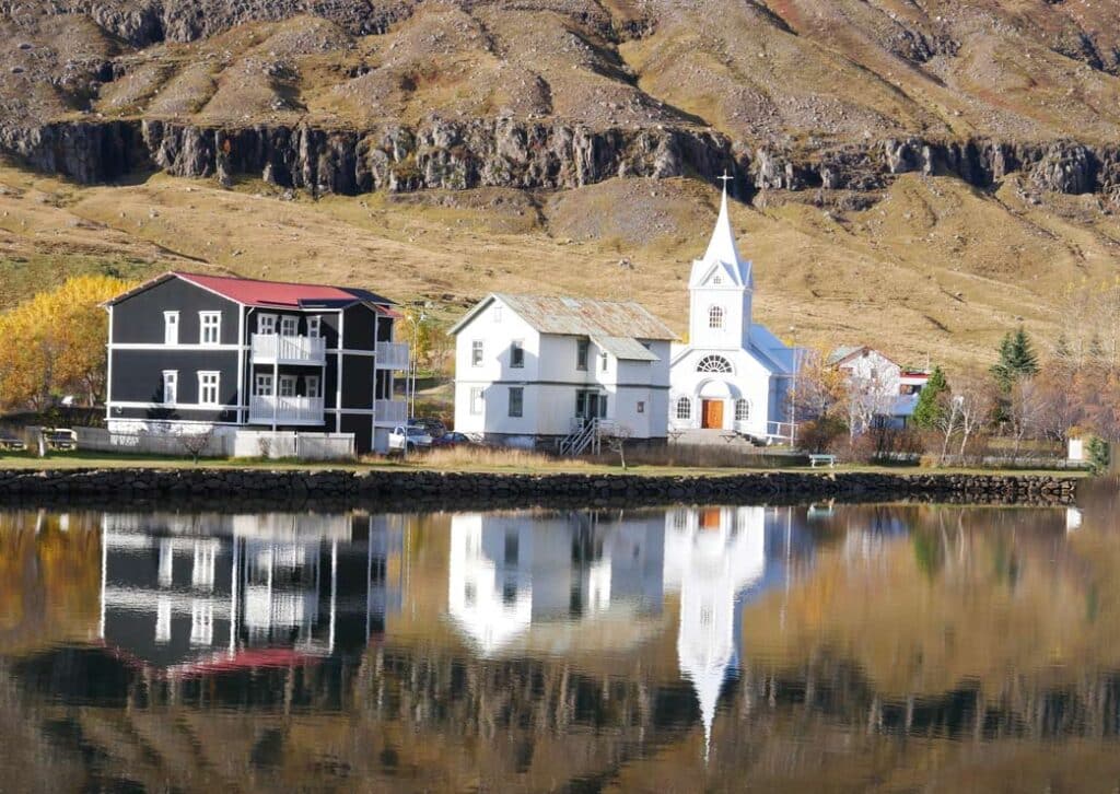 weiße kirche in ostisland spiegelt sich im fjord