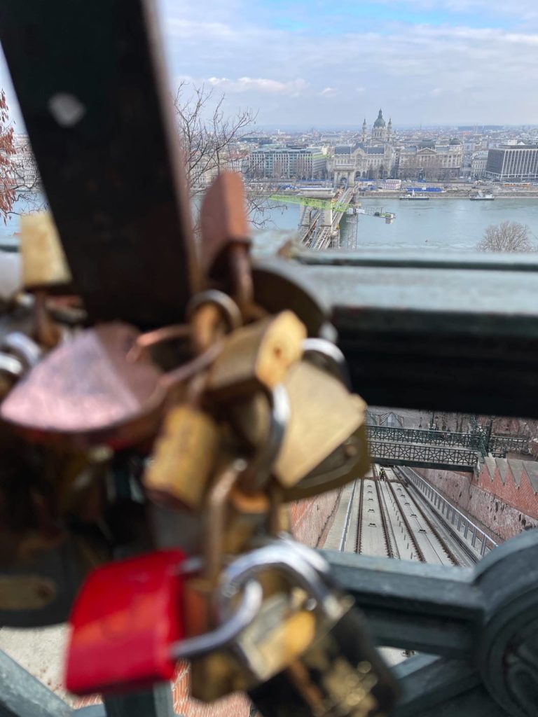 nahaufnahme-von-liebesschlössern-im-hintergrund-blick-auf-das-parlament-in-budapest