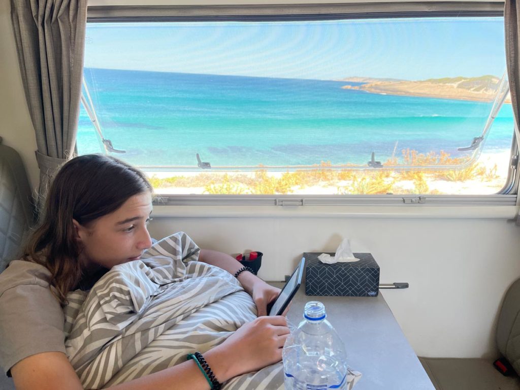 Ultimativer Guide für den Westaustralien Roadtrip teenager-liest-auf-ebook-im-wohnmobil-vor-dem-fenster-traumstrand-in-australien