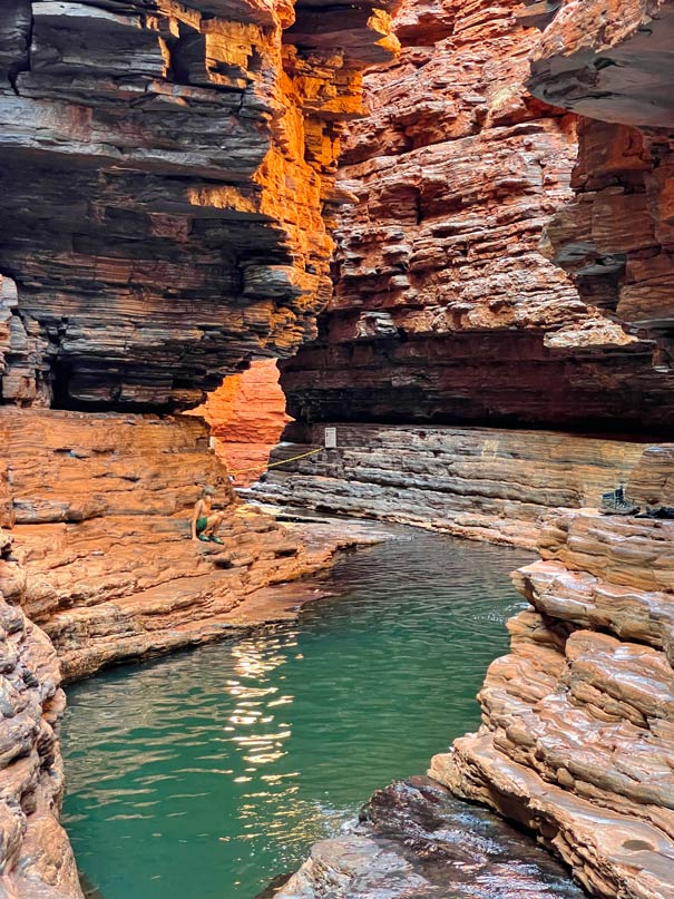 kind-sitzt-im-roten-sandstein-slot-canyon-vor-einem-gruenen-wasserpool-im-karijini-nationalpark