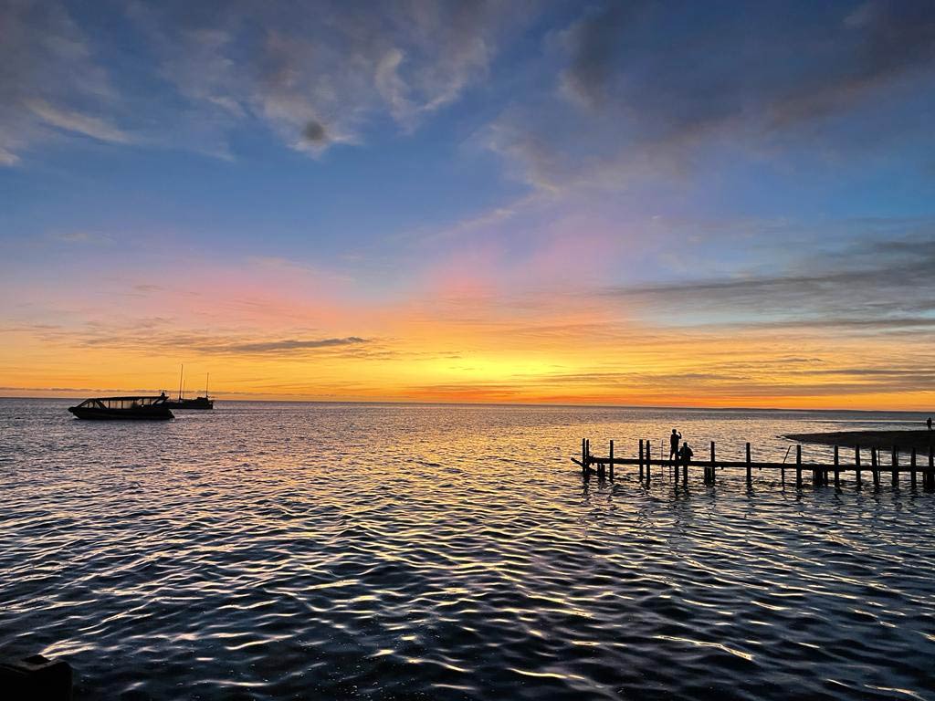 sonne-geht-ueber-dem-meer-in-monkey-mia-auf-man-sieht-das-meer-und-den-orange-farbenen-himmel-ein-pier-ragt-von-rechts-in-das-bild-und.links-liegt-ein-boot-im-wasser