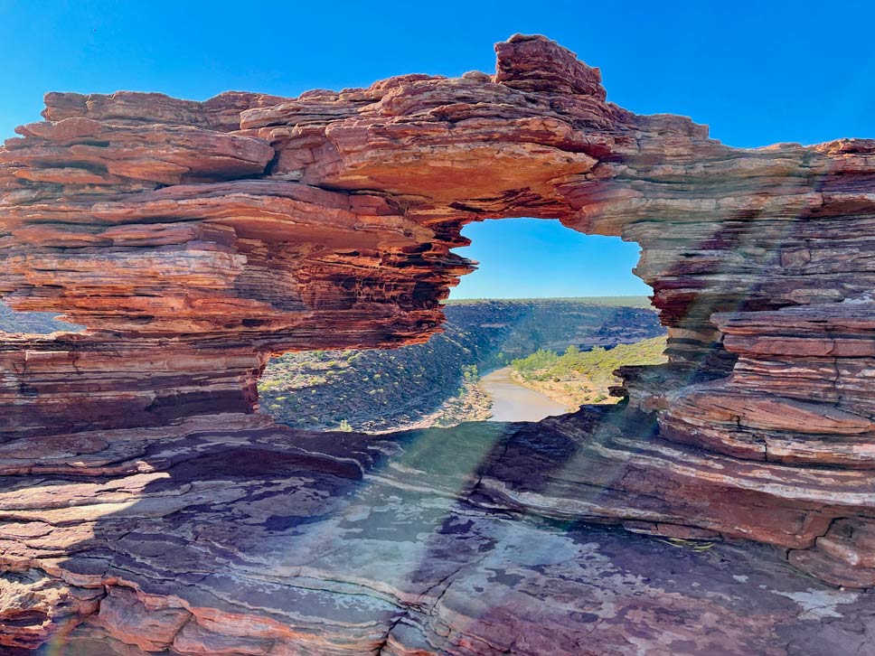 rote-sandstein-formation-die-sich-schichtet-und-wie-ein-fenster-durch-ein-loch-den-blick-auf-den-fluss-freigibt