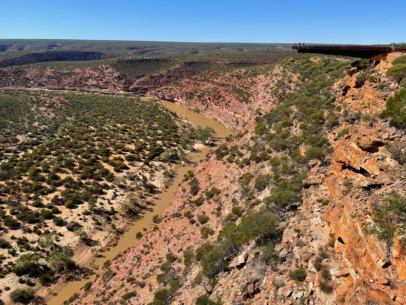 rote-sandstein-landschaft-mit-begruenten-bereichen-am-fluss-rechts-oben-ragt-ein-brauner-skywalk-ins-bild