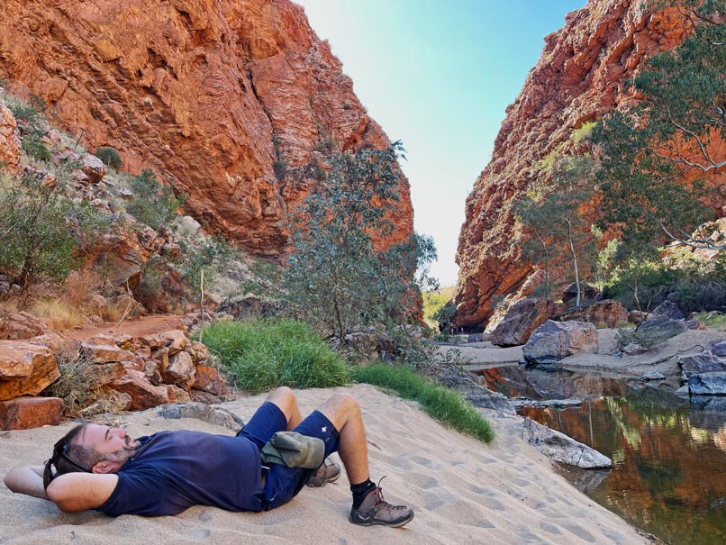 Roadtrip Northern Territory - Rundreise von Darwin zum Uluru mann-liegt-auf-sandbank-zwischen-roter-schlucht-im-west-macdonnell-nationalpark