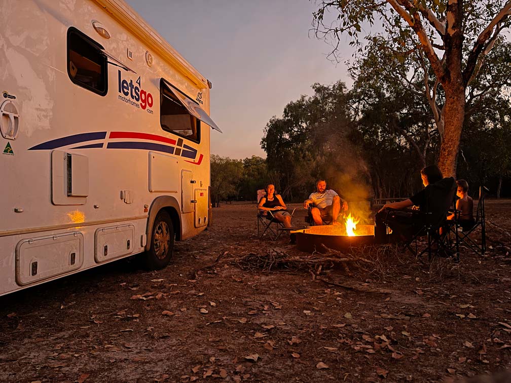 Roadtrip Northern Territory - Rundreise von Darwin zum Uluru familie-sitzt-in-der-daemmerung-am-lagerfeuer-neben-wohnmobil-in-australien