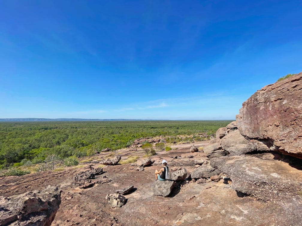Roadtrip Northern Territory - Rundreise von Darwin zum Uluru frau-sitzt-auf-felslandschaft-und-blickt-ueber-den-gruenen-busch-im-kakadu-nationalpark