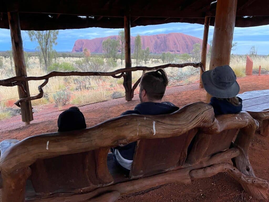 familie sitzt auf bank und blickt auf uluru