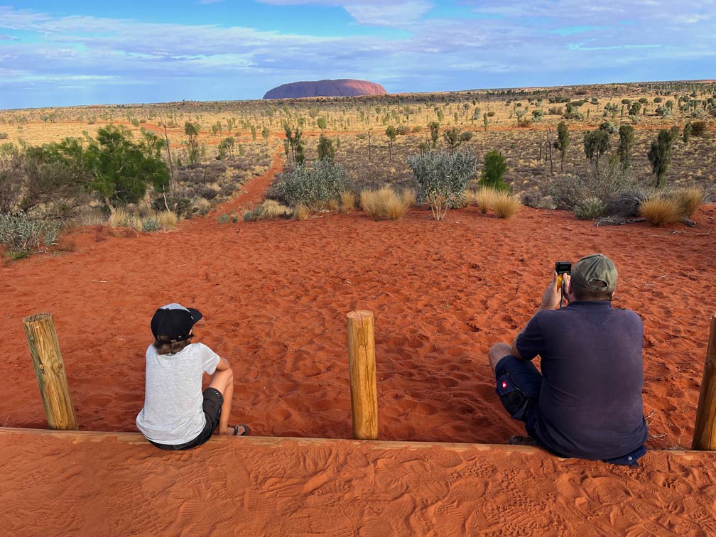 Roadtrip Northern Territory - Rundreise von Darwin zum Uluru vater-und-sohn-sitzen-im-roten-sand-und-blicken-auf-uluru