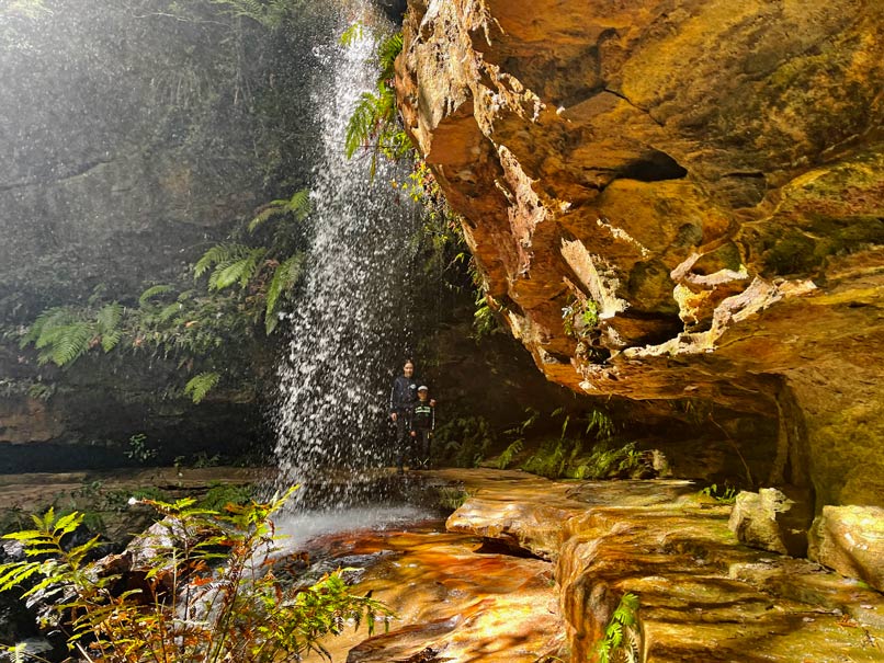 zwei-kinder-hinter-wasserfall-am-felsvorsprung-in-den-blue-mountains