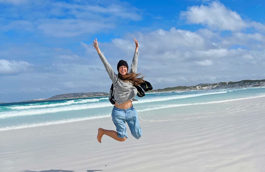 jenni von der strandfamilie hüpft an weißem sandstrand in australien in die luft