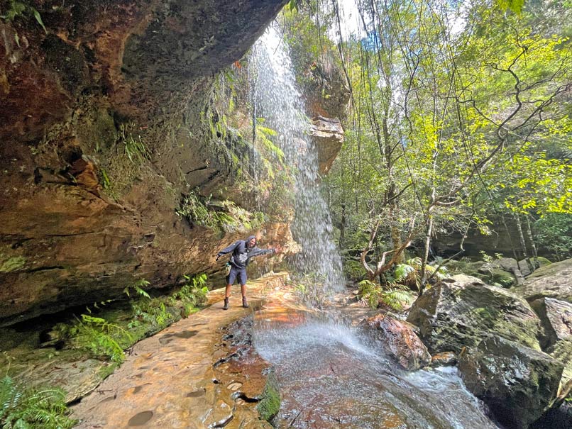 mann-laueft-hinter-wasserfall-am-grand-canyon-track-in-den-blue-mountains-entlang