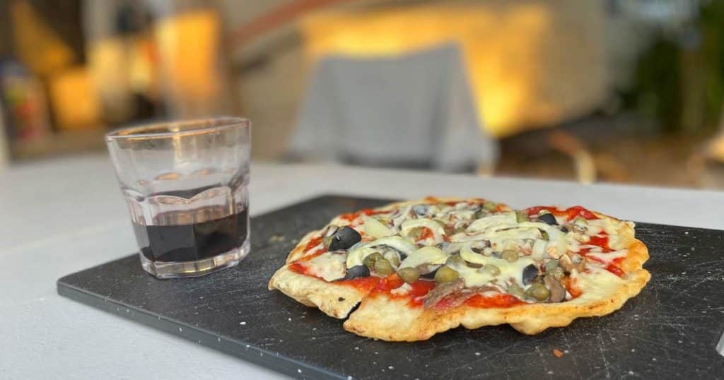 pizza auf einem brett daneben ein glas rotwein im hintergrund ein camper in dem dieses rezept gekocht wurde