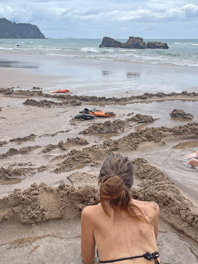 frau-liegt-in-heisser-quelle-am-sandstrand-mit-blick-aufs-meer-am-hot-water-beach-neuseeland