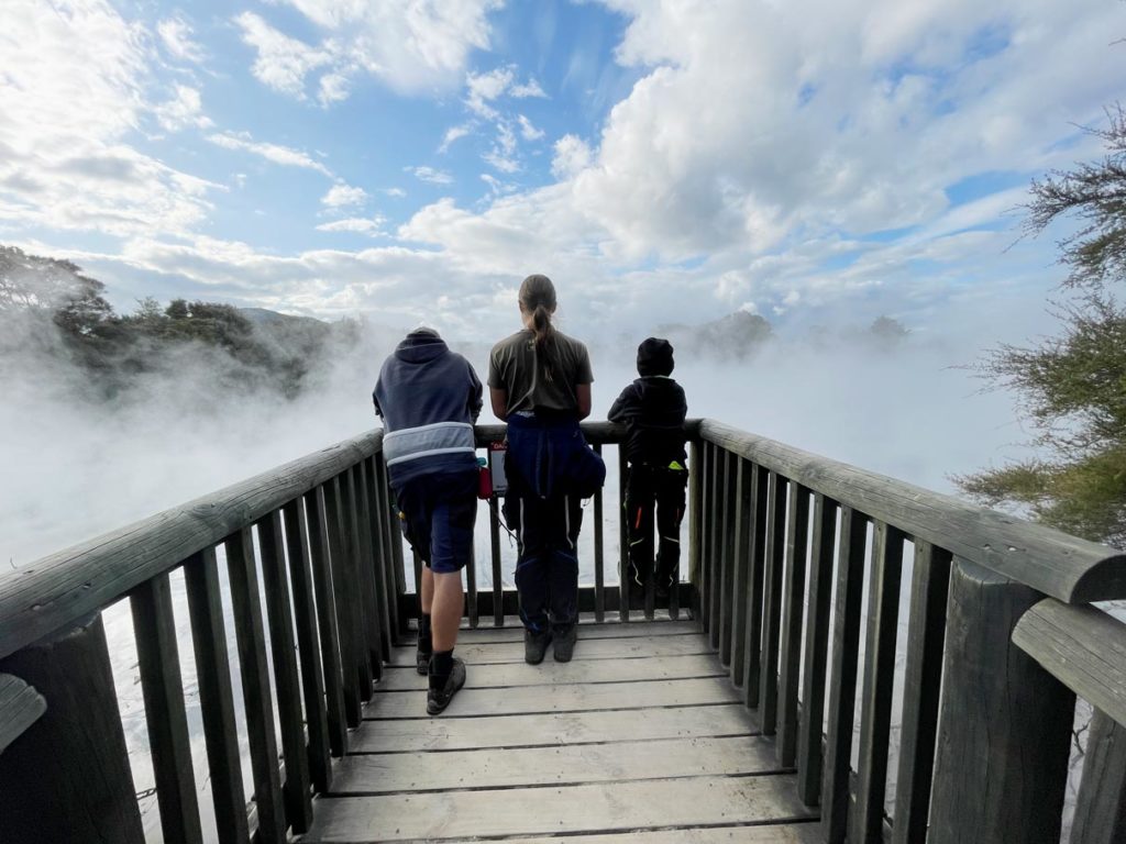 vater-mit-kindern-auf-steg-ueber-geothermalen-gebiet-rotorua-kuriau-park