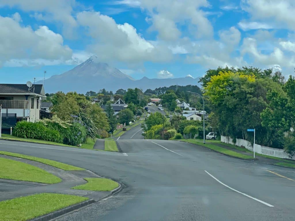 strasse-in-new-plymouth-neuseeland-durch-die-stadt-mit-haeusern-und-gruenen-gaerten-im-hintergrund-vulkan-taranaki