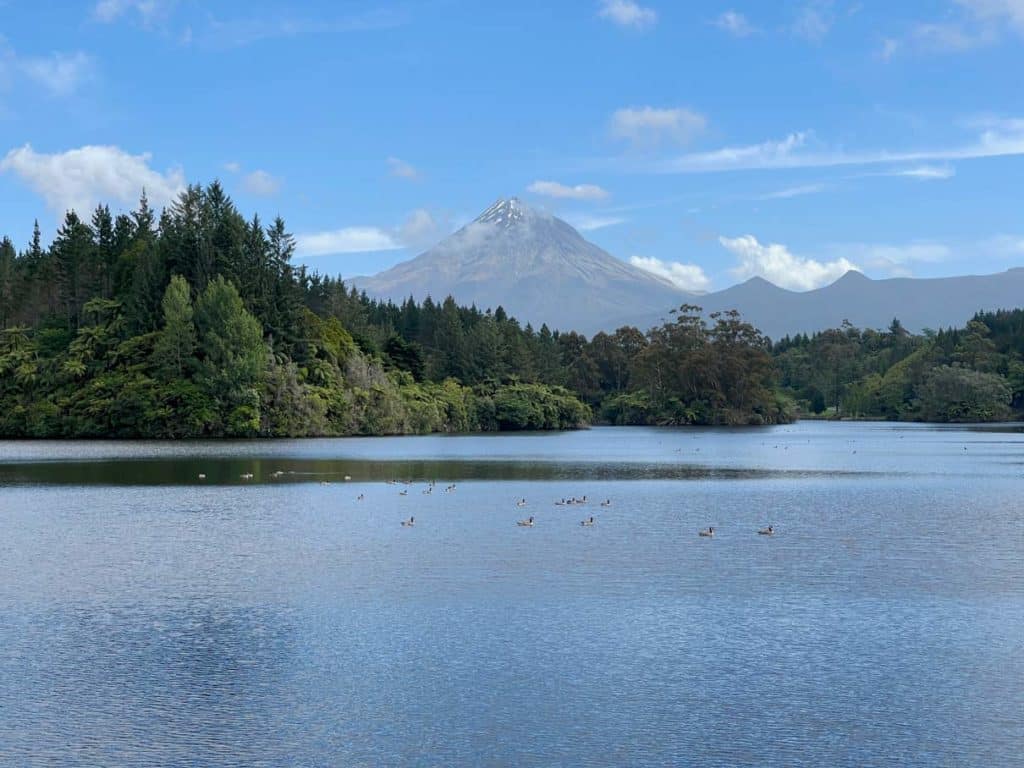 blauer-see-lake-mangamahoe-dahiner-gruener-wald-und-mittig-der-vulkan-taranaki-in-neuseeland