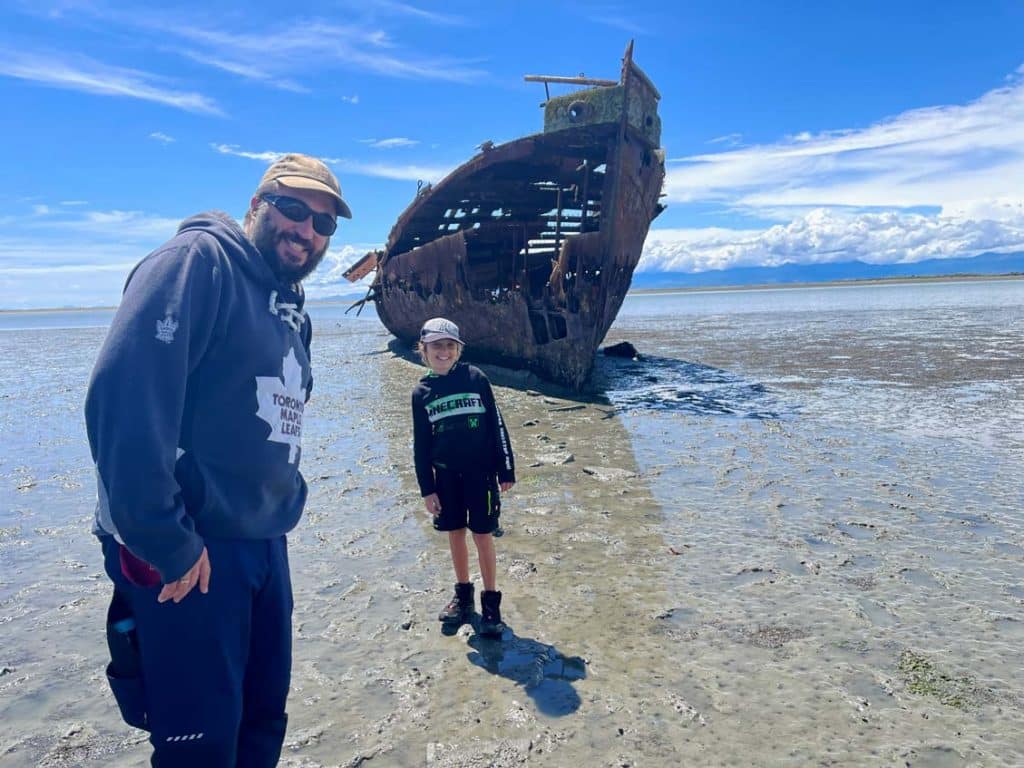 vater-und-sohn-stehen-bei-ebbe-am-strand-vor-einem-schiffswrack-auf-der-suedinsel-neuseeland