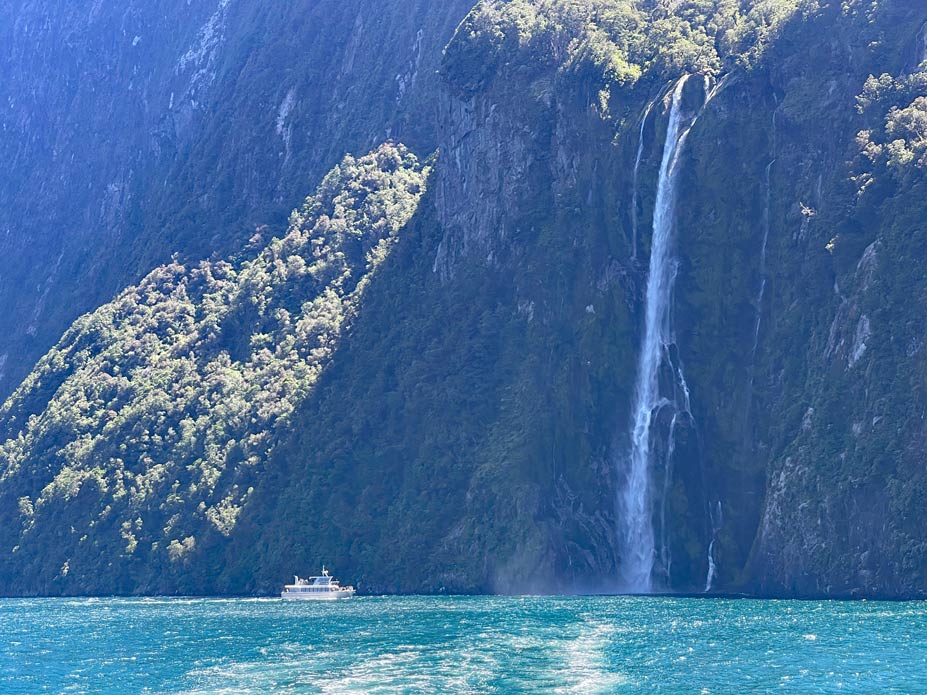 boot-naehert-sich-wasserfall-der-sich-von-der-hohen-felswand-im-milford-sound-ergiesst