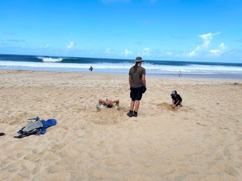 familie-am-sandstrand-mit-blick-auf-surfer-hawaii