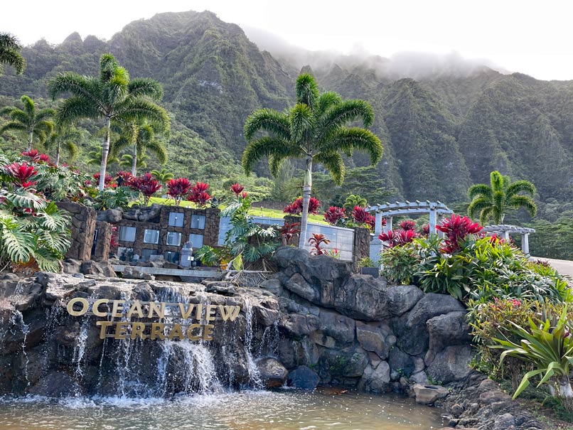 inschrift-valley-of-the-temples-oahu-mit-palmen-auf-stein-und-wasserfall-vor-bergkette