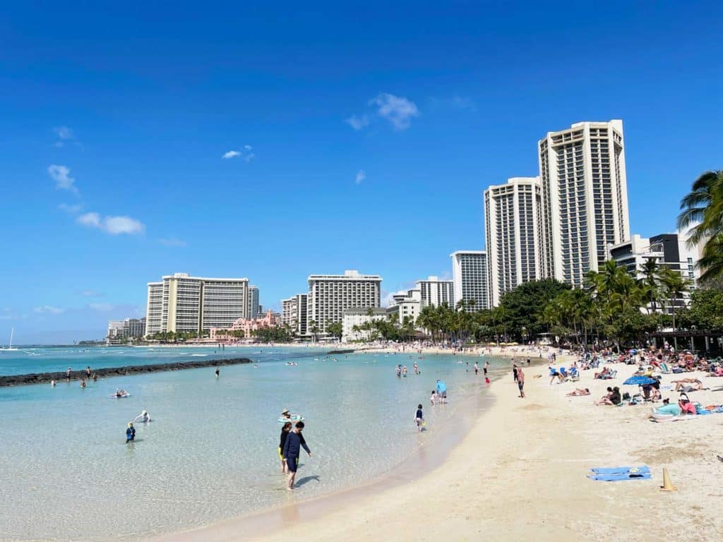 hellblaues-wasser-in-geschuetzer-bucht-am-waikiki-beach-heller-sandstrand-und-wolkenkratzer