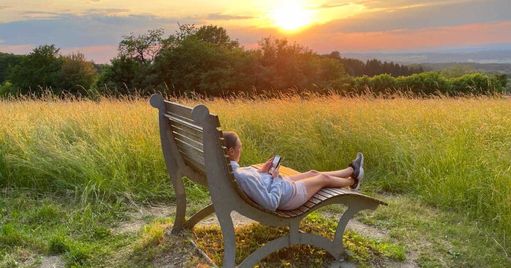 frau-liegt-auf-Bank-lernt-auf-handy-fremdsprache-im-Sonnenuntergang-fremdsprachen-fuer-urlaub-lernen