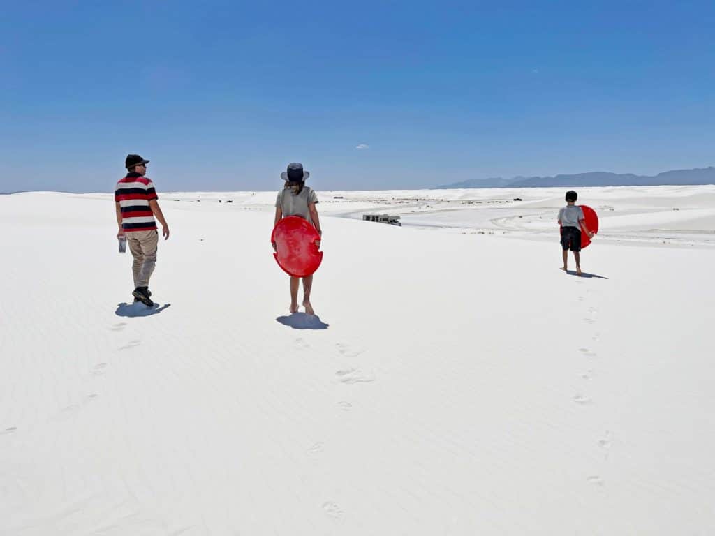 vater-und-kinder-laufen-mit-schlitten-ueber-weisse-sandduenen-zum-wohnmobil-white-sands-nationalpark-camper-roadtrip-usa