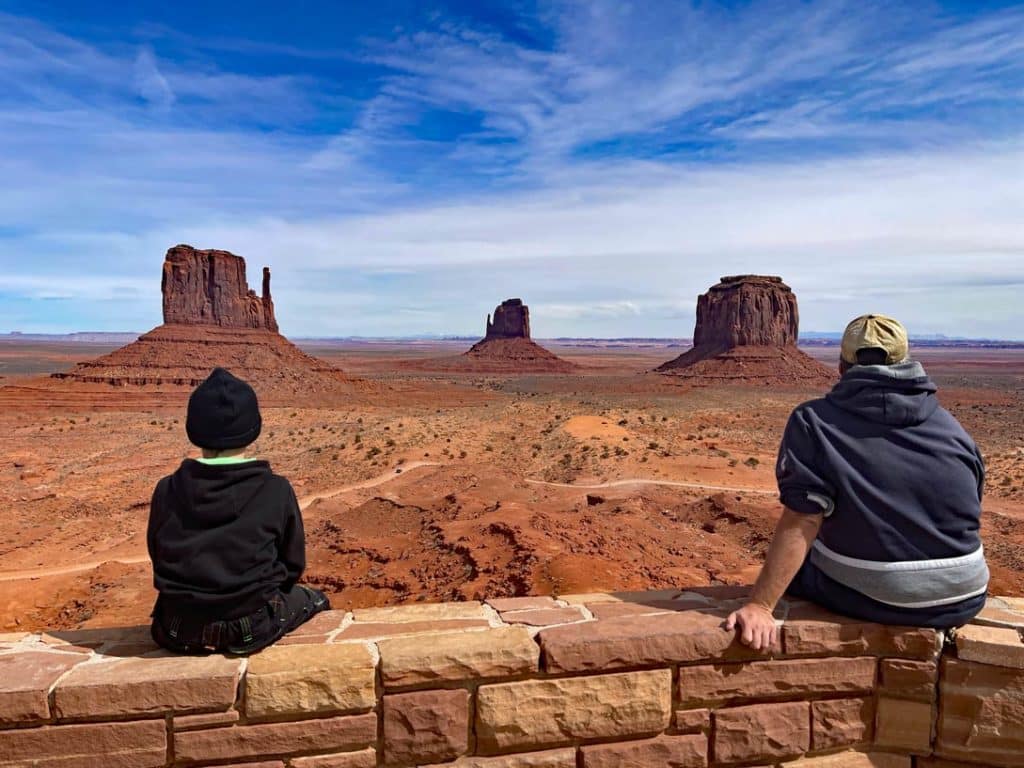 vater-und-sohn-sitzen-auf-mauer-und-blicken-auf-die-roten-butts-im-monument-valley