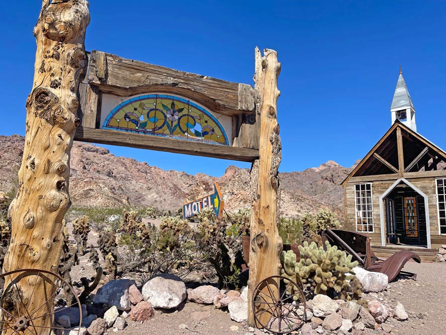 holzschild-zwischen-kakteen-neben-alter-kirche-in-nelsons-ghosttown