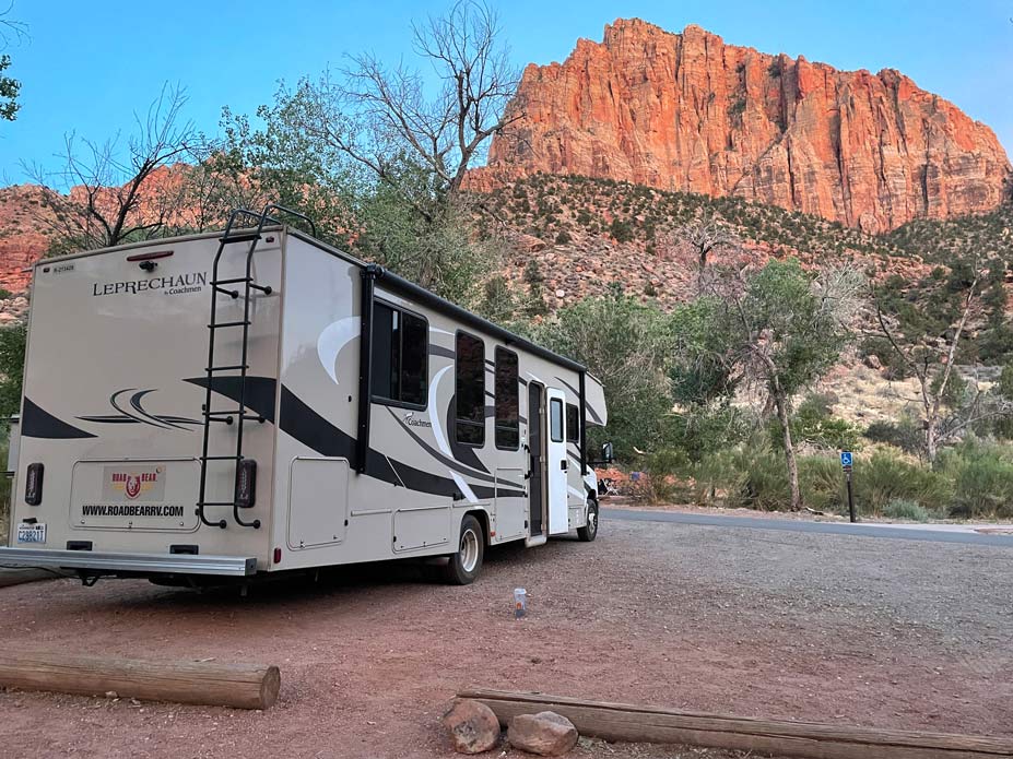 grosses-wohnmobil-steht-auf-watchman-campingplatz-im-zion-nationalpark-mit-blick-auf-rote-felsen