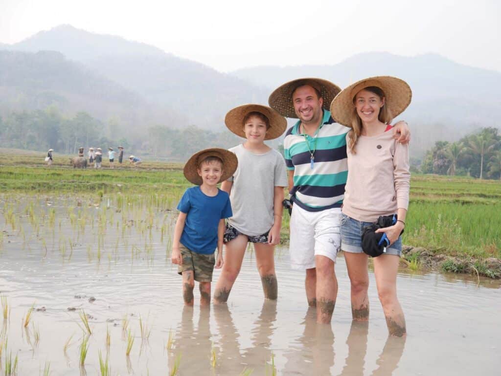 familie-steht-in-reisfeld-in-laos-mit-strohhueten-auf-dem-kopf-waehrend-familienweltreise