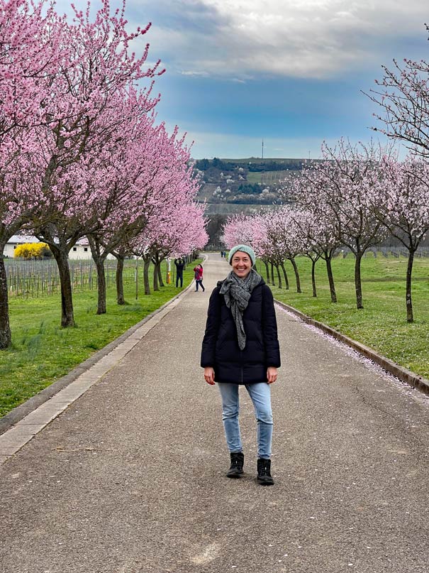 jenni-von-der-strandfamilie-steht-auf-allee-zwischen-bluehenden-mandelbaeumen