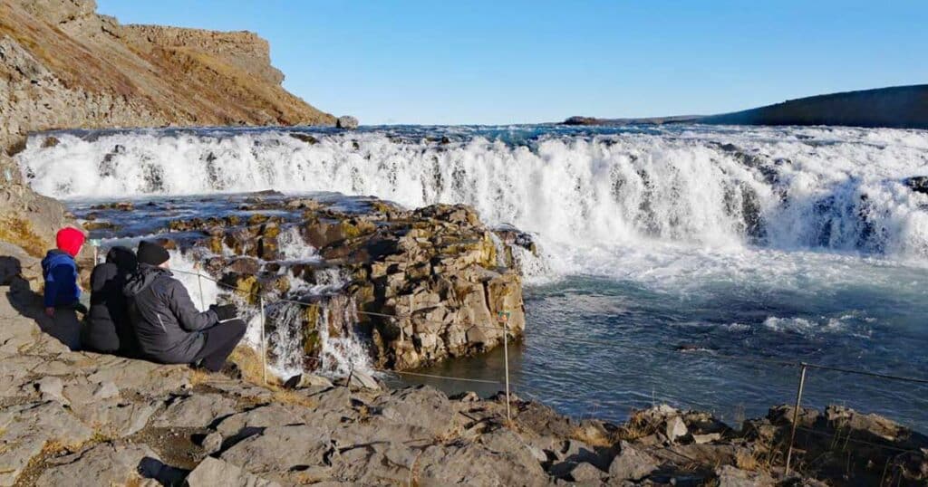 Familie sitzt auf Steinen vor Wasserfall Gullfoss am Golden Circle auf Island