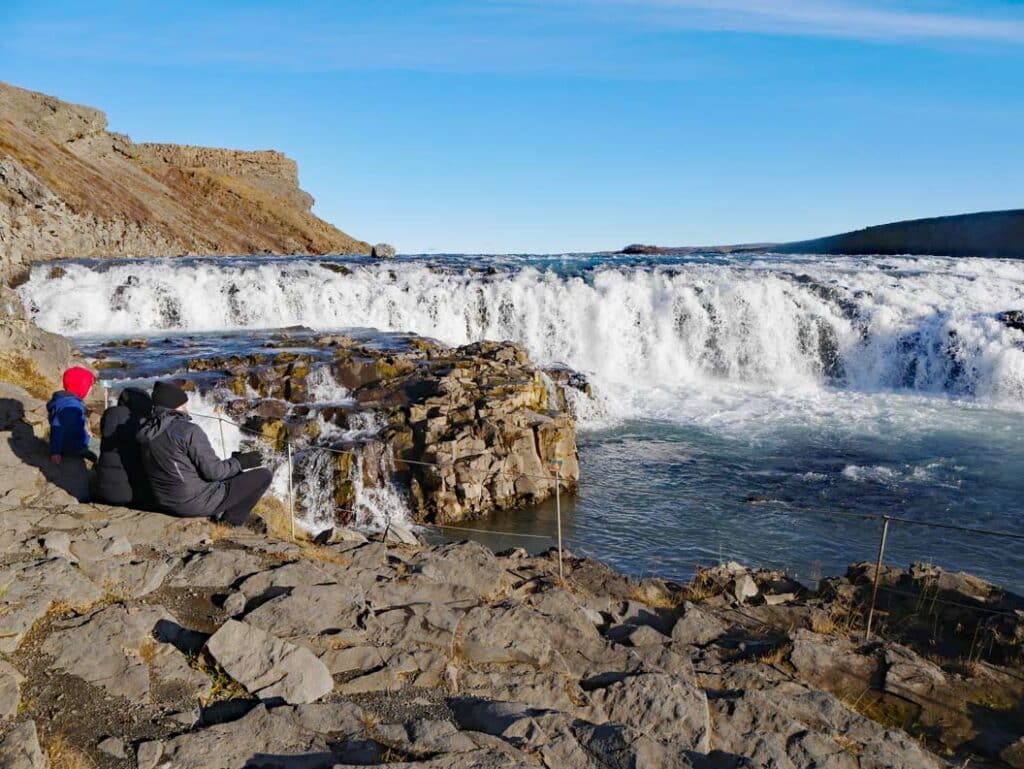 Golden Circle Island - 3+ Island Highlights auf einer Route familie-sitzt-auf-steinen-vor-gullfoss-wasserfall