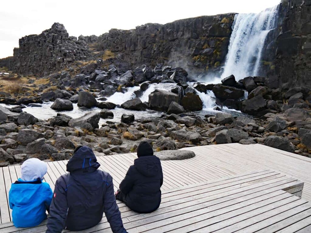 Golden Circle Island - 3+ Island Highlights auf einer Route familie-sitzt-auf-holzboden-vor-wasserfall-im-thingvellir-nationalpark