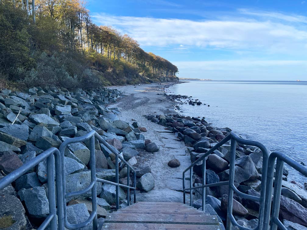 holzsteg-mit-treppe-fuehrt-an-strand-mit-vielen-steinen-in-heiligendamm-am-wald