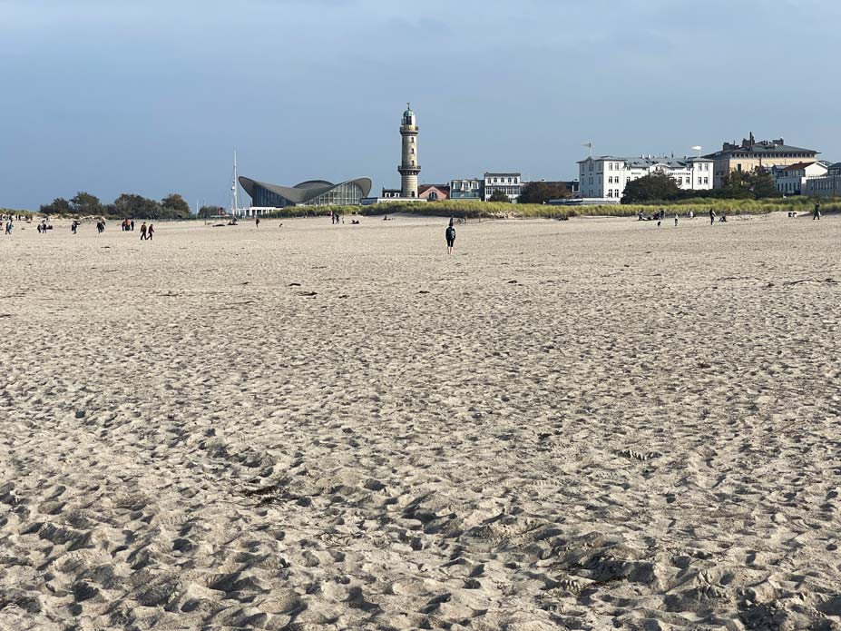 heller-sandstrand-im-hintergrund-leuchtturm-von-warnemuende-und-teepott