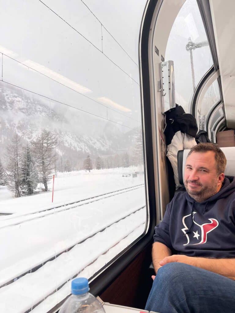Bernina Express vs. Regionalbahn: Tipps für die perfekte Zugreise durch die Schweizer Alpen mann-sitzt-im-erste-klasse-abteil-bernina-express-im-panoramawagen-in-verschneiter-landschaft