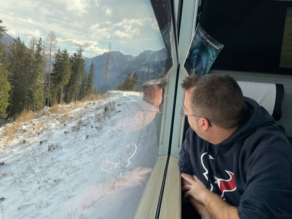 Bernina Express vs. Regionalbahn: Tipps für die perfekte Zugreise durch die Schweizer Alpen mann-blickt-aus-zug-auf-bernina-express-strecke-im-schnee